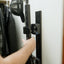 Person adjusting a mounted rifle against a white wall.